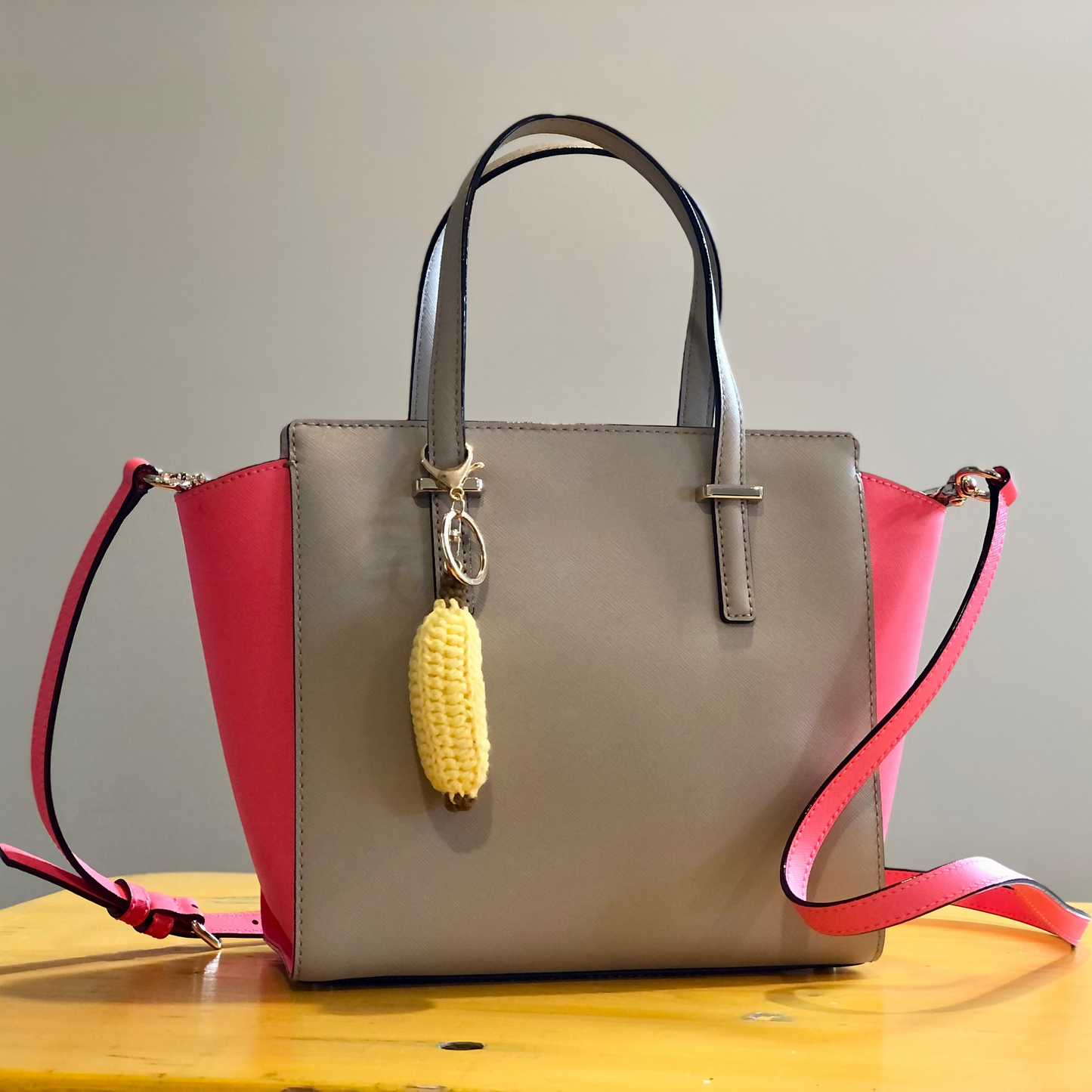 A crocheted handbag charm in the shape of a banana attached to a handbag.