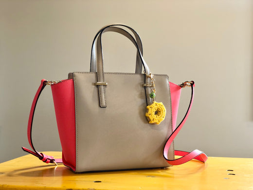 Handbag sitting on table with a crocheted donut handbag charm attached