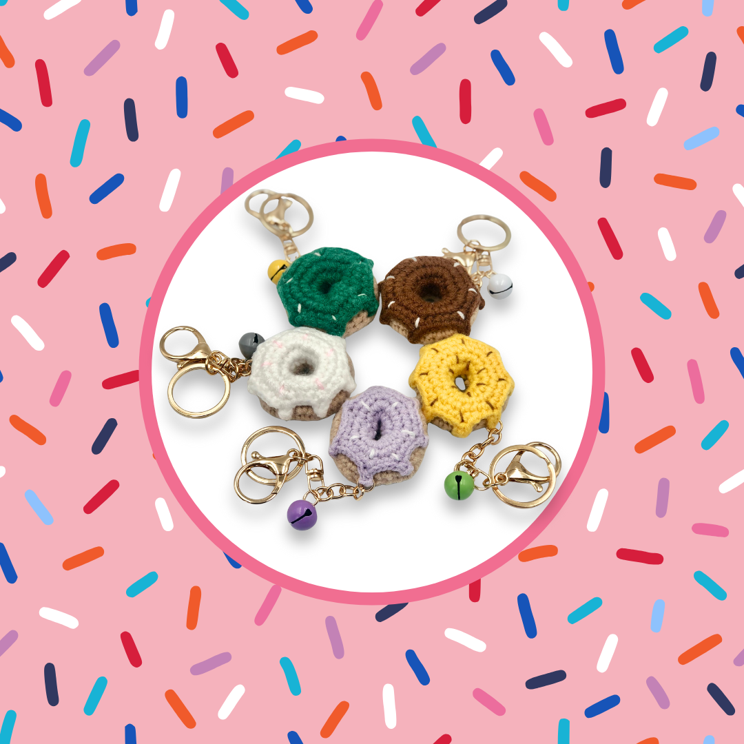 Five colourful donut-shaped crochet handbag charms on a pink background with sprinkles pattern