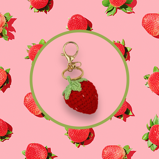 Strawberry-shaped crochet handbag charm on a pink background with strawberry pattern