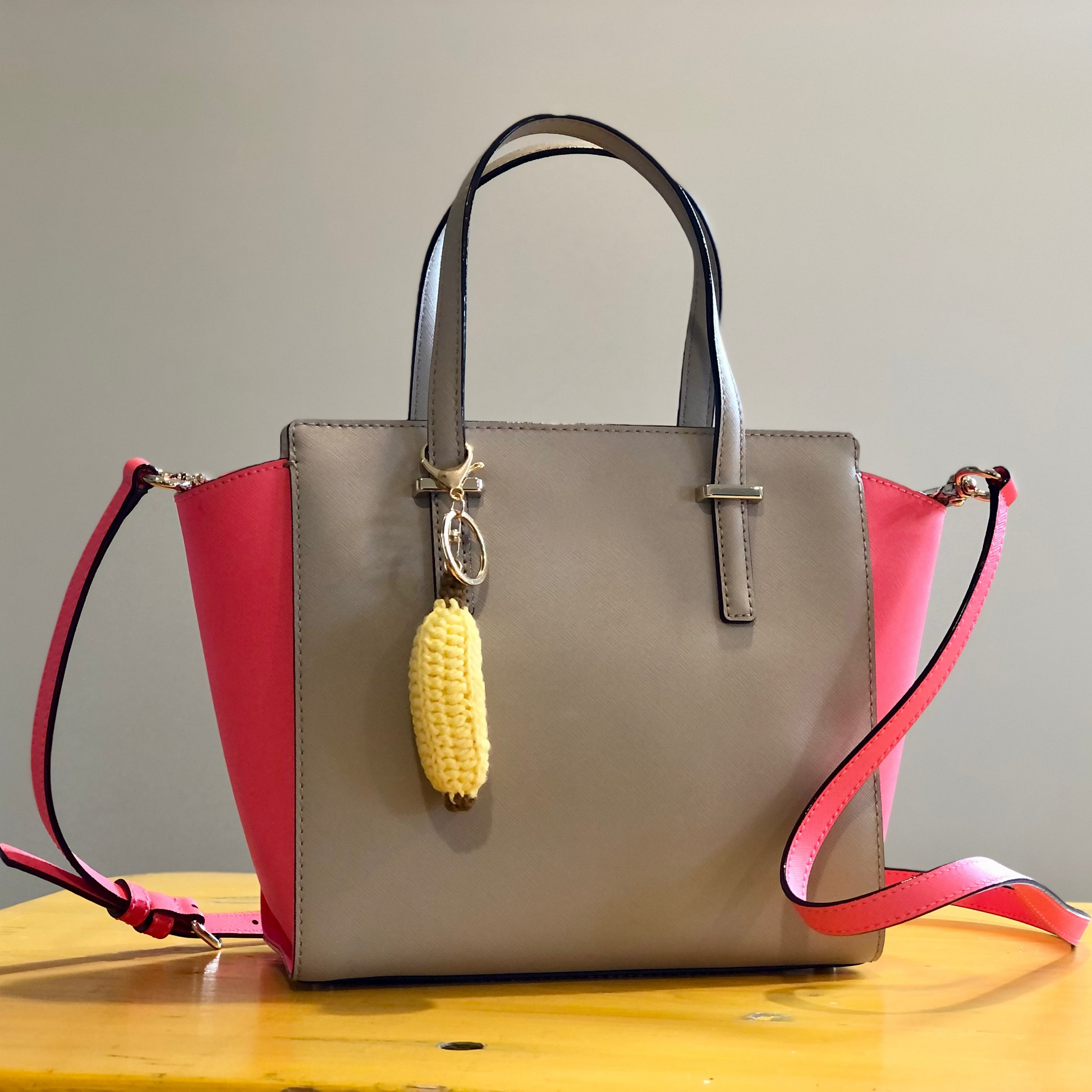 A crocheted handbag charm in the shape of a banana attached to a handbag.