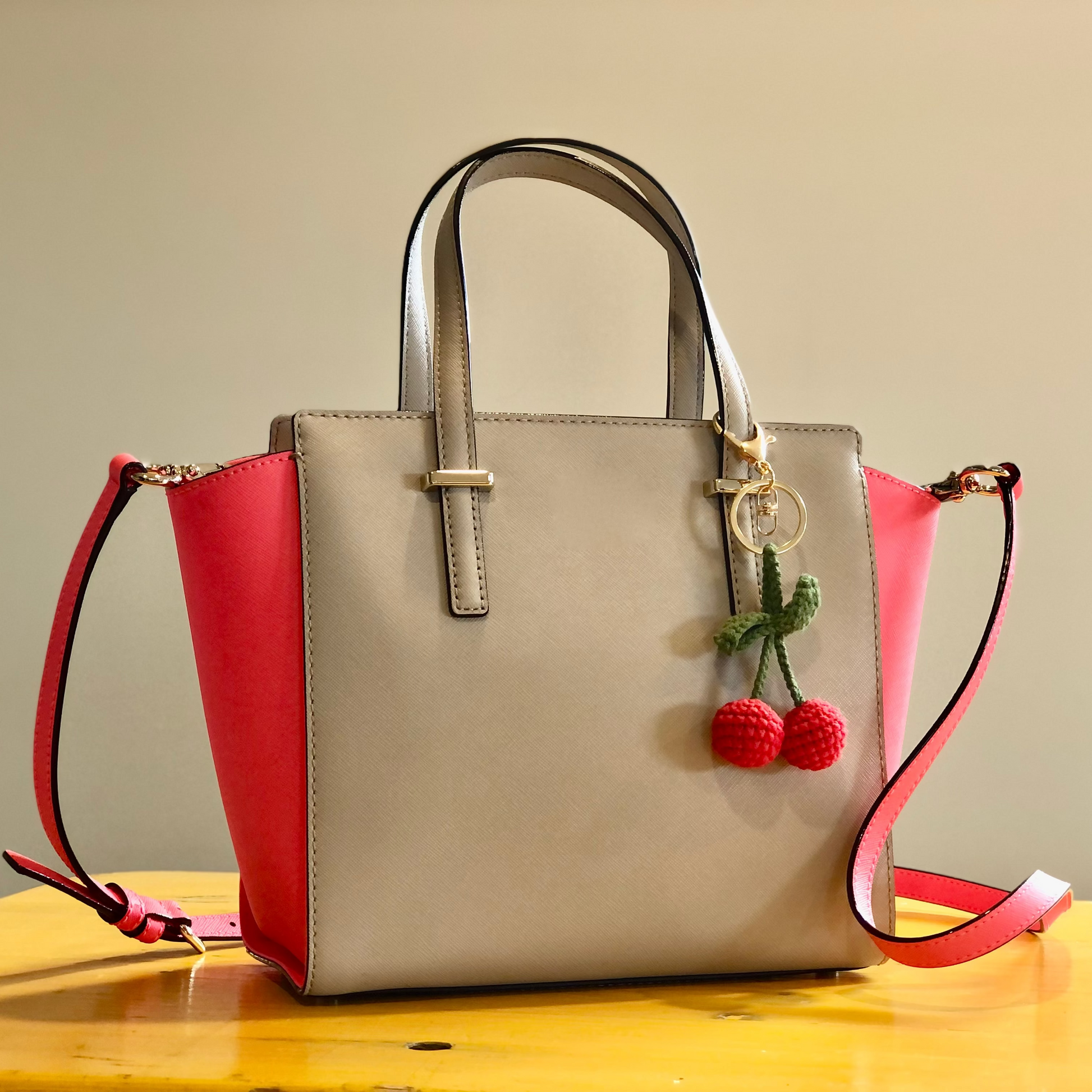 A crocheted handbag charm in the shape of a cherry attached to a handbag.