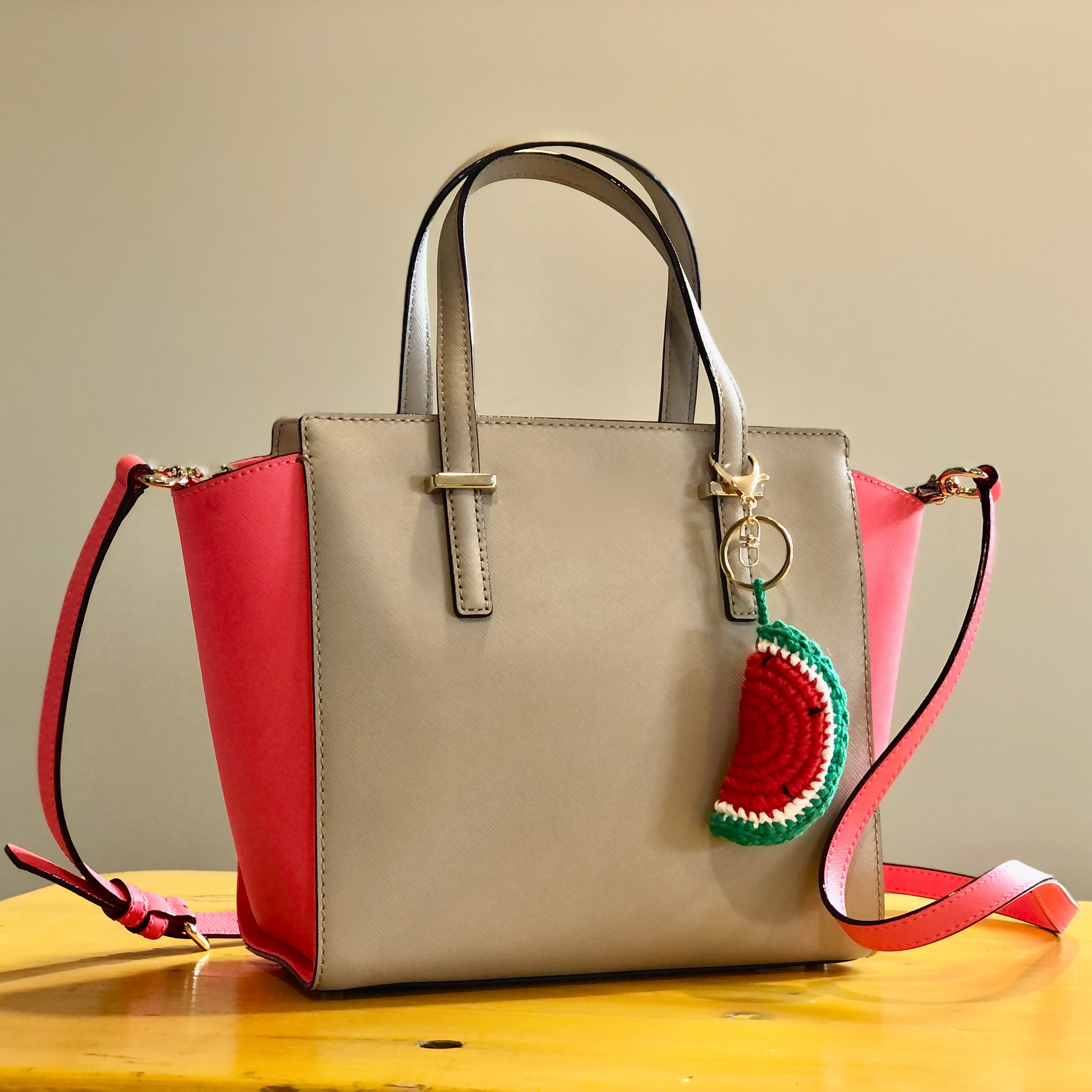 A crocheted handbag charm in the shape of a slice of watermelon attached to a handbag.