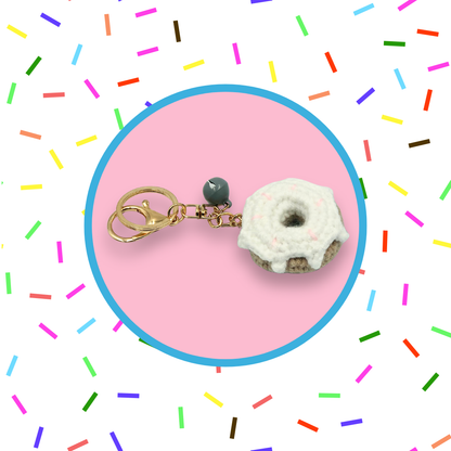 White donut-shaped crochet handbag charm on a pink background with sprinkles pattern